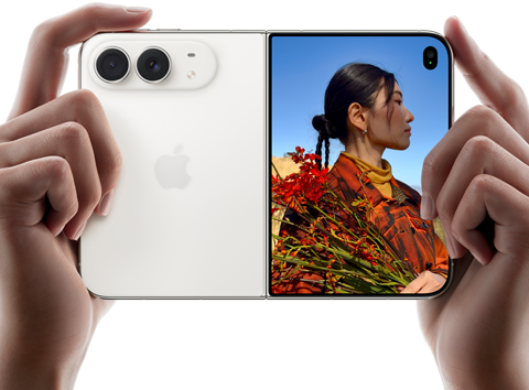 جهاز iPhone Duo، لون أبيض النجوم، يدان تحملان الجهاز في الوضع الأفقي، مفتوح، اللوحة اليسرى تعرض الكاميرا المزدوجة 48MP Fusion الخلفية، اللوحة اليمنى تعرض شخصاً تُلتقط صورته على الشاشة الخارجية، يمكن لهذا الشخص رؤية وجهه لأن الصورة تُلتقط باستخدام ميزة Duo Preview